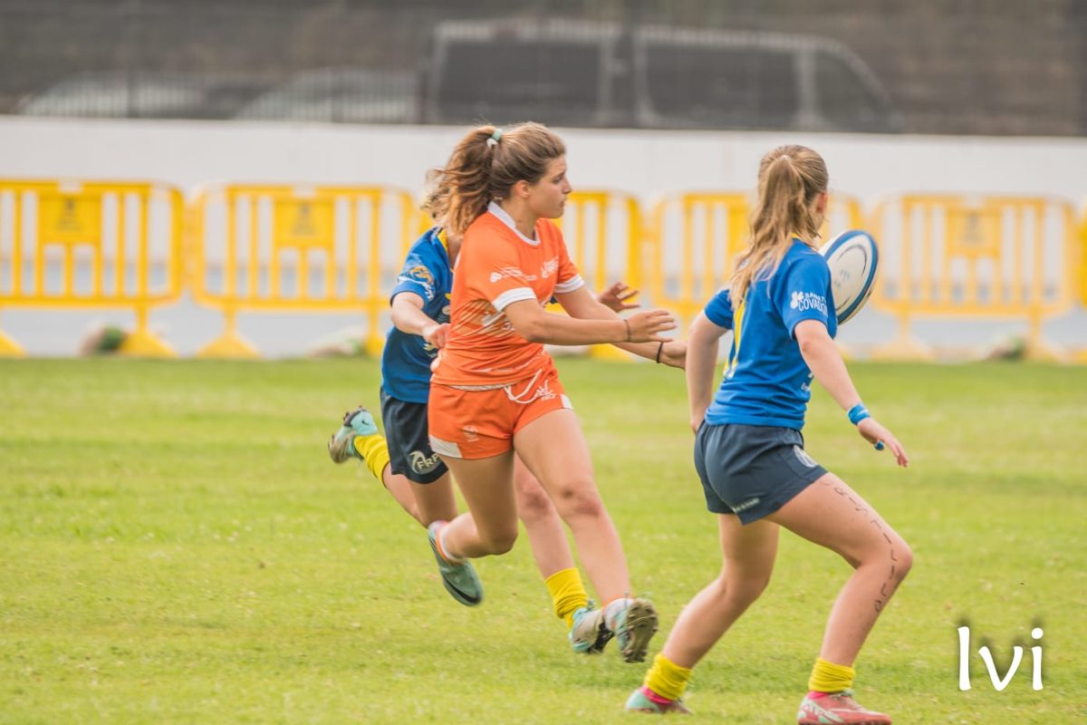 Jugadora de naranja da un pase en carrera ante la defensa rival durante un partido de rugby femenino